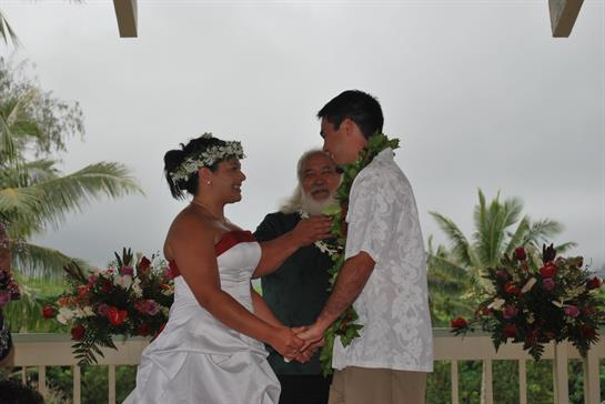 Wedding ceremony takes place outdoors with a couple holding hands and smiling in Hawaii.