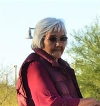 An elderly woman wearing sunglasses and a red vest enjoys a peaceful day outdoors among greenery.