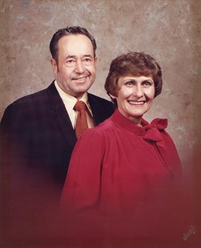 A smiling couple stands side by side, dressed in formal attire, celebrating a memorable moment.