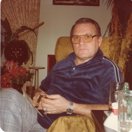 A man relaxes in an armchair, dressed casually and sipping a drink among plants.