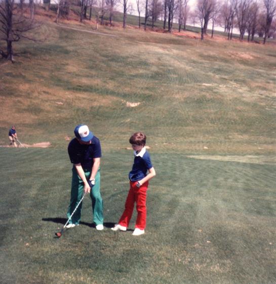 Father teaches son golf on a sunny day at a local course, creating lasting memories.