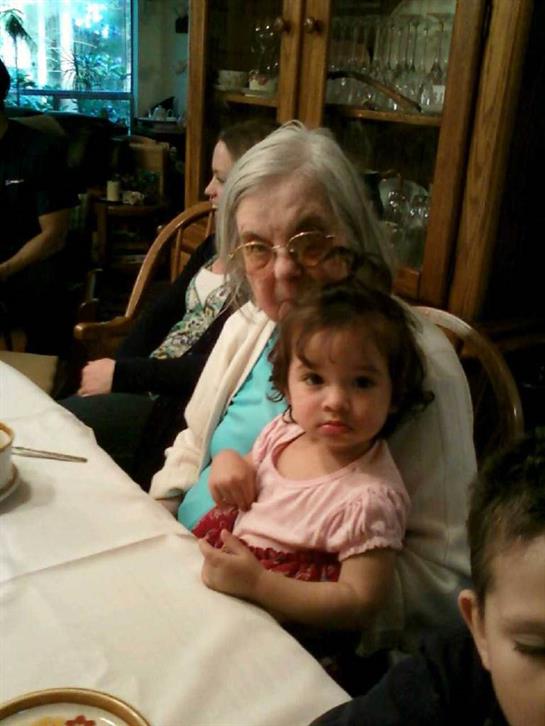 A grandmother and granddaughter share smiles and food at a family dinner.