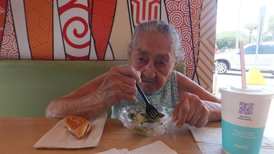 An elderly woman is eating a fresh salad in a lively restaurant full of patterned decor.