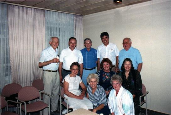 A group of twelve friends poses together, smiling in a well-lit indoor space during a reunion.