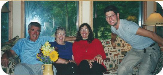 Three people smile and pose for a group photo inside a cozy living room filled with natural light.