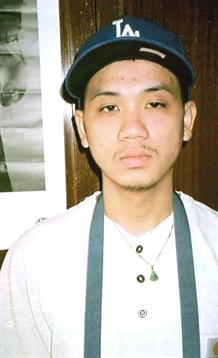Young individual poses in a cozy café, wearing an apron and cap, looking directly at the camera.
