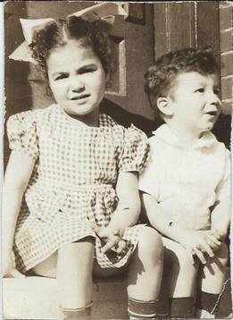 Two children sit side by side on a porch, smiling and enjoying their time outdoors in daylight.