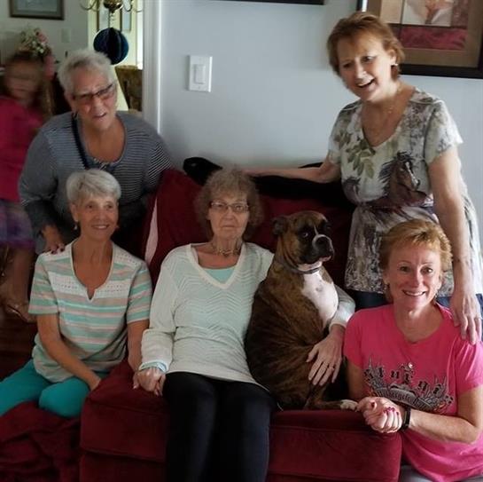 A group of women sits on a couch, smiling and enjoying time together with a dog.