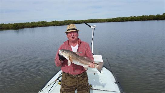 Fisherman showcases a large catch while standing on a boat in serene waters with lush surroundings.