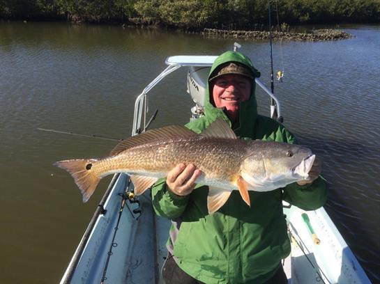 A happy angler proudly holds a sizable redfish on a small boat in calm waters.