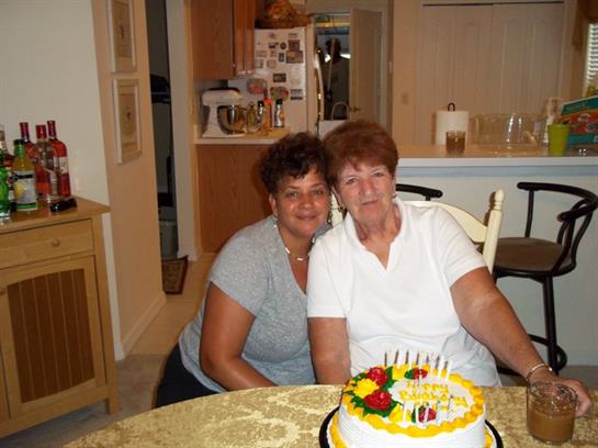 Two friends celebrate a birthday, smiling by a decorated cake in a cozy kitchen.