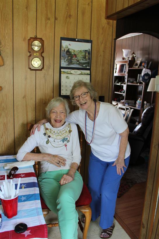 Two elderly women share a moment of laughter in a warm, inviting living room filled with memories.
