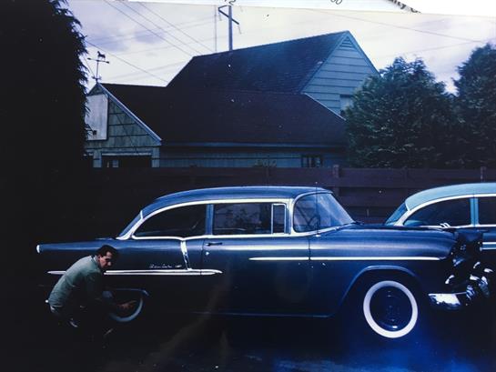 A vintage car is being repaired in a suburban neighborhood as dusk approaches.
