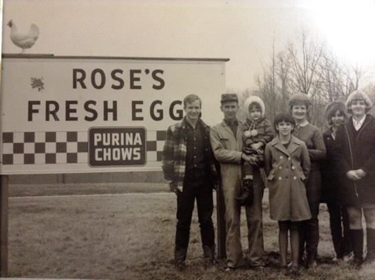 Five people gather by a farm sign promoting fresh eggs for the cold weather.