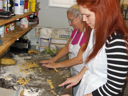 Women roll out dough and shape pasta in a warm kitchen, enjoying quality time and culinary skills.