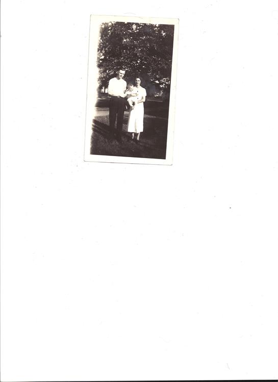 A couple poses together in a lush garden, enjoying a sunny day, showcasing mid-century fashion.