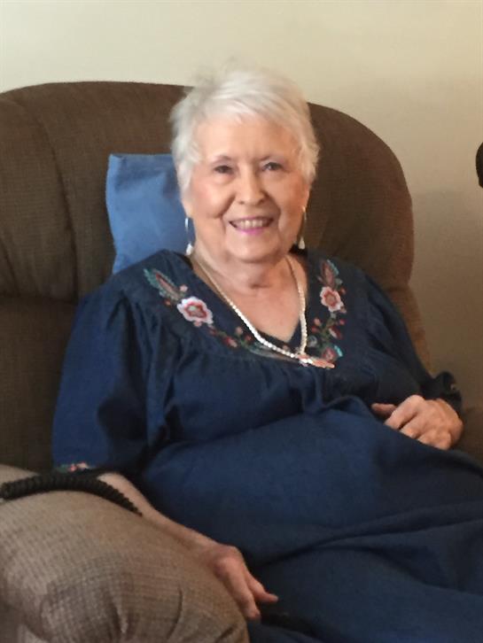 An older woman enjoys her time sitting in a cozy chair, smiling and relaxed in her home.