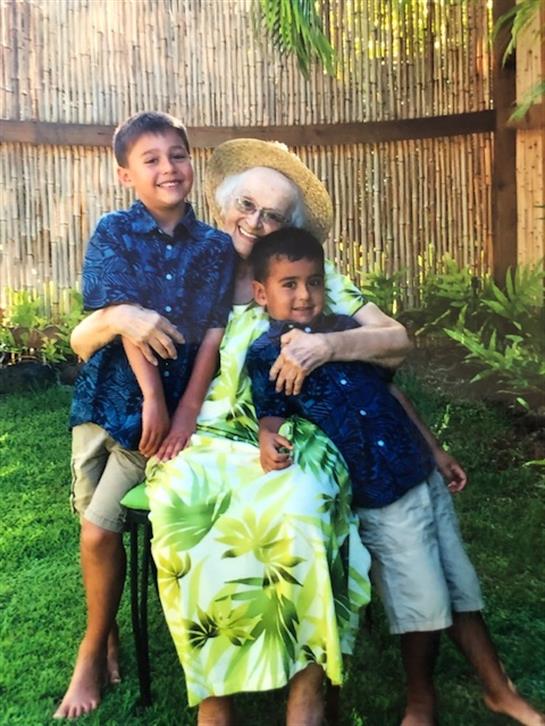 Grandmother relaxes outdoors with her two cheerful grandchildren surrounded by lush plants.