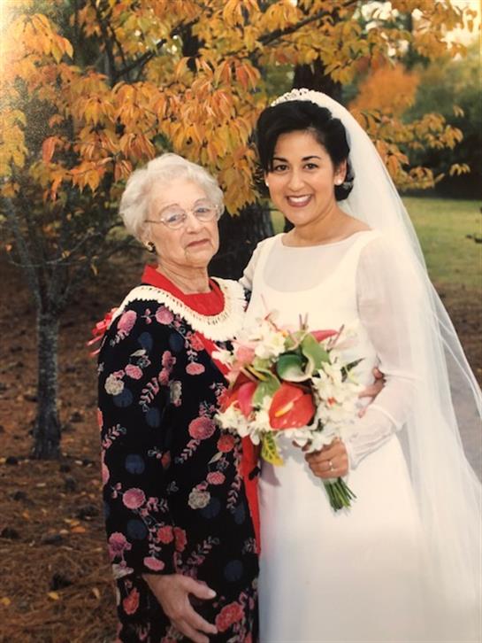 Two women stand together with smiles, showcasing a beautiful wedding bouquet in a park.