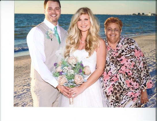 A couple poses with a family member on the beach during their wedding celebration at sunset.