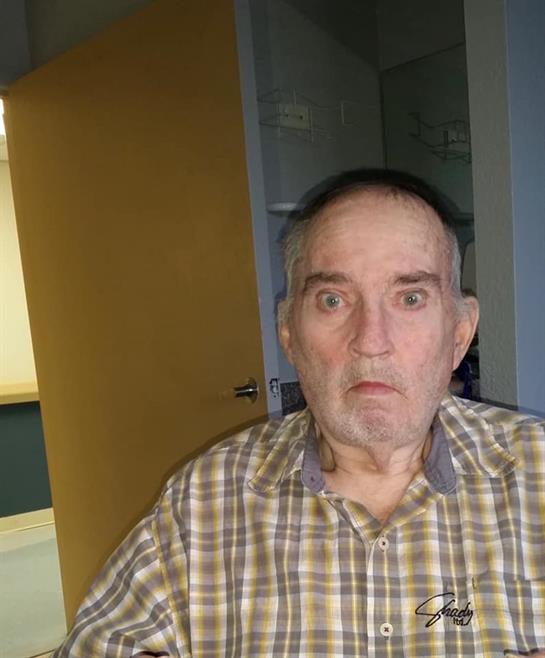 An elderly man displays a surprised look while seated in a well-lit room, suggesting curiosity.