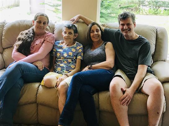 Four family members relax and share smiles on a couch in a warmly lit living room.