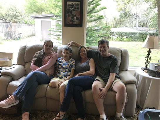 Four family members relax together on a soft couch in a bright living room.