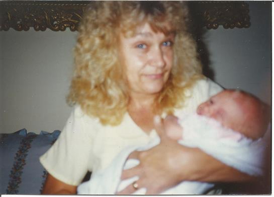 A woman with curly hair lovingly holds a baby in her arms, radiating warmth in daylight.