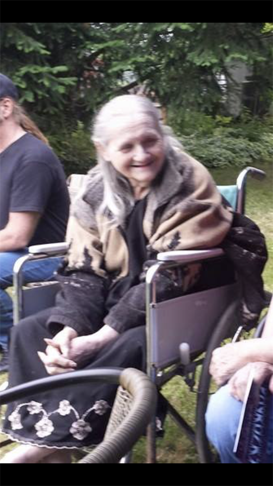 An elderly woman in a wheelchair smiles warmly while others share moments in the sun.