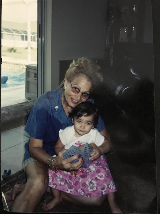 A loving grandmother holds her young granddaughter close, both smiling happily indoors.