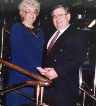 A couple stands together on a cruise ship's staircase, dressed formally, sharing a joyful moment.