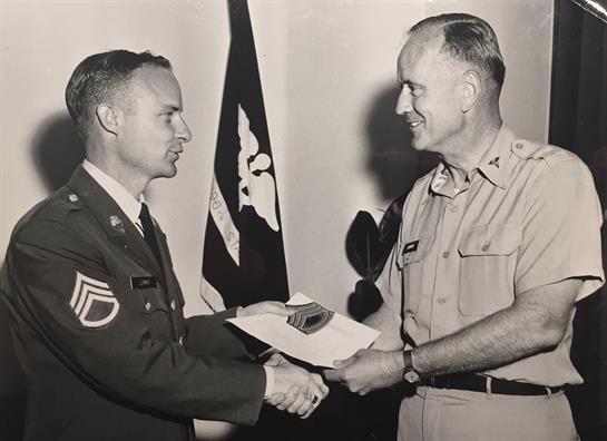 Two military officers shake hands while exchanging rank insignia in an official ceremony.