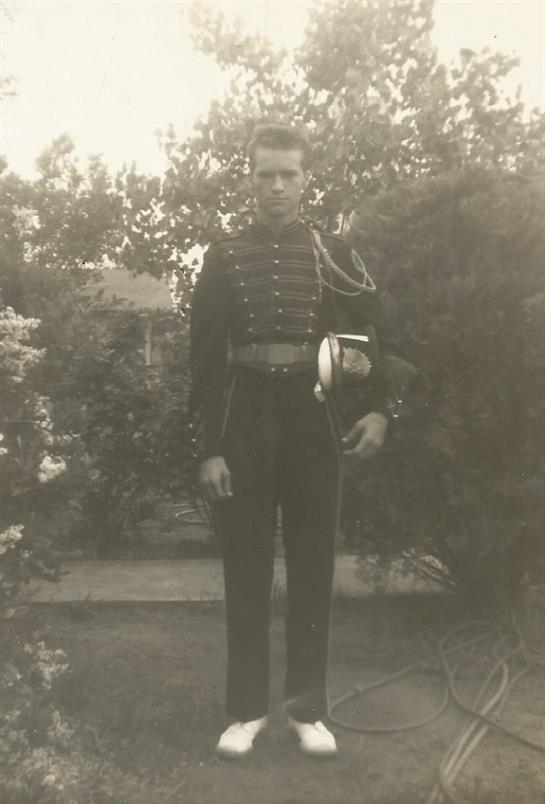 Individual dressed in a historical military uniform poses in a lush garden setting.