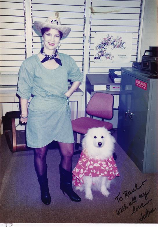 A woman stands proudly in a stylish outfit beside a fluffy dog in a playful dress.