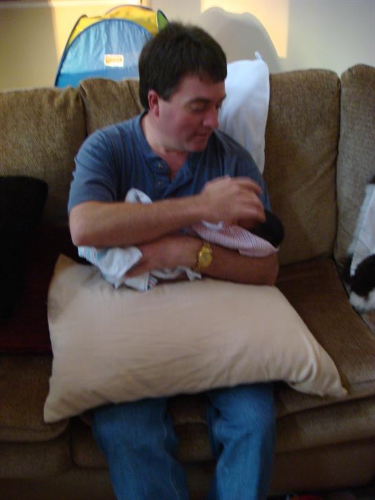 A father gently holds and cares for his newborn baby while sitting on a couch.