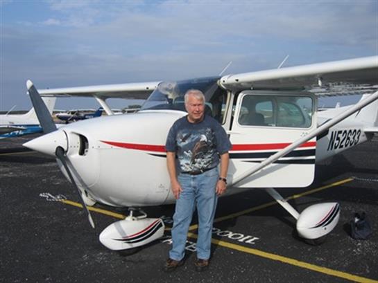 A man poses beside a small aircraft on the tarmac, showcasing his joy and passion for flying.