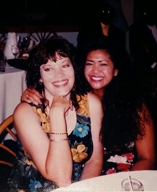 Two women share smiles and laughter during a lively gathering in a festive atmosphere.