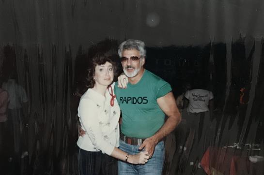 A man and woman dance closely, dressed in vintage clothing, at a fun event in the 1980s.