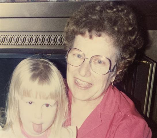 A cheerful grandmother and her playful granddaughter smile and pose in a warm living room.