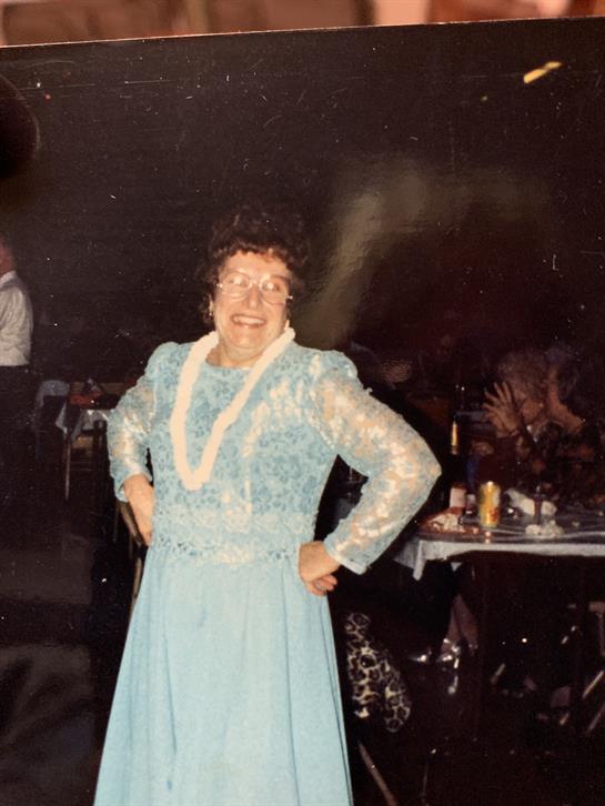 An elderly woman in a blue dress dances happily at a party.