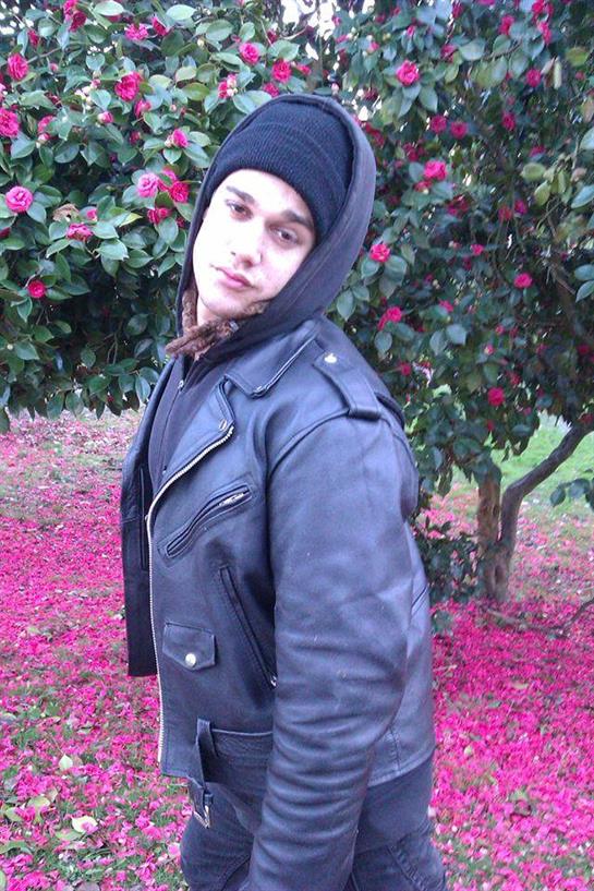 A young man stands confidently among vibrant flowers in a park during springtime.