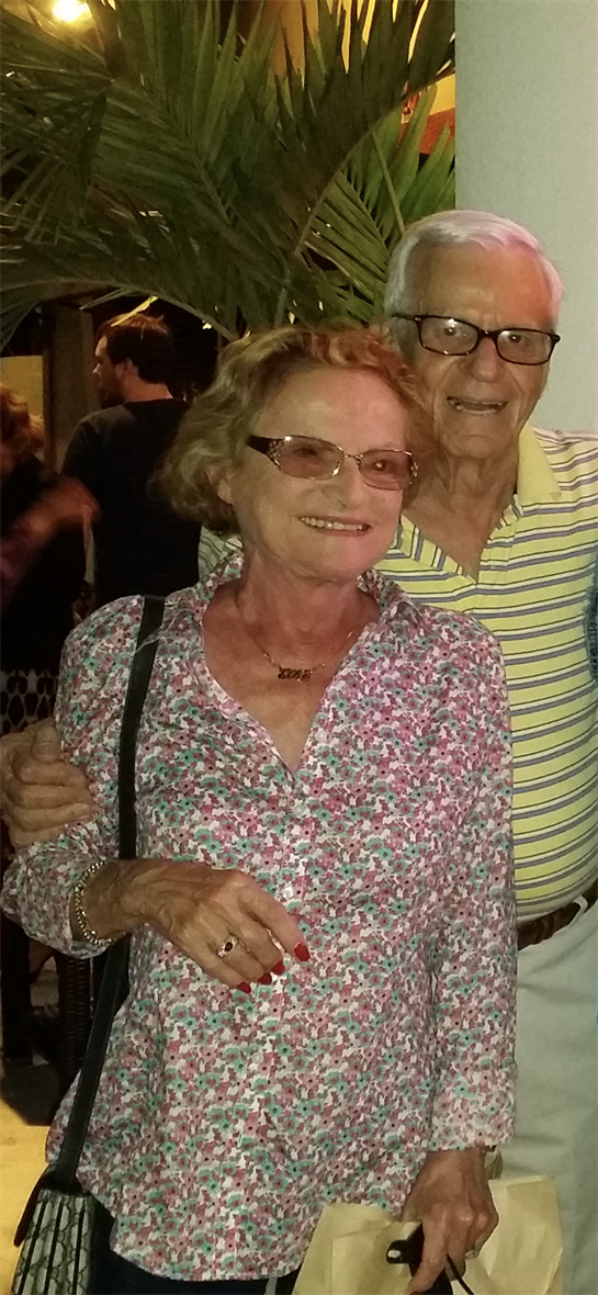 Two seniors smile warmly while celebrating with friends in a festive gathering at night.