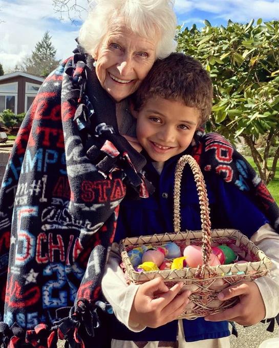 An elderly woman and a boy happily hold a basket of decorated eggs wrapped in a blanket.