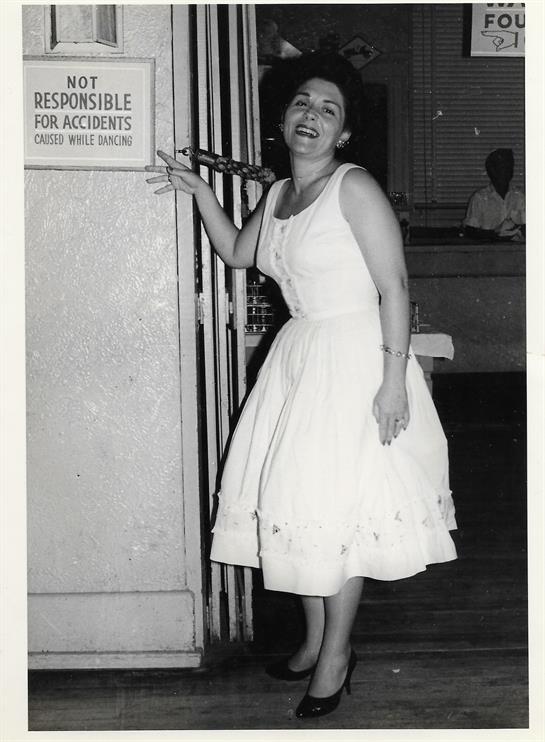 A woman in a white dress smiles playfully at a building entrance during an evening event.