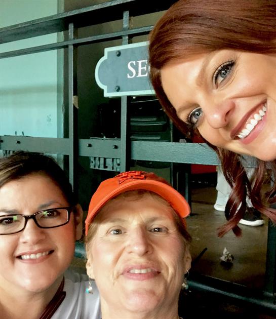 Three friends are smiling joyfully while posing together at a lively cafe setting.