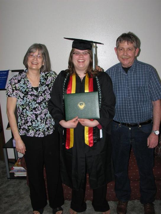 Family members proudly pose with a recent graduate holding her diploma and wearing a cap.