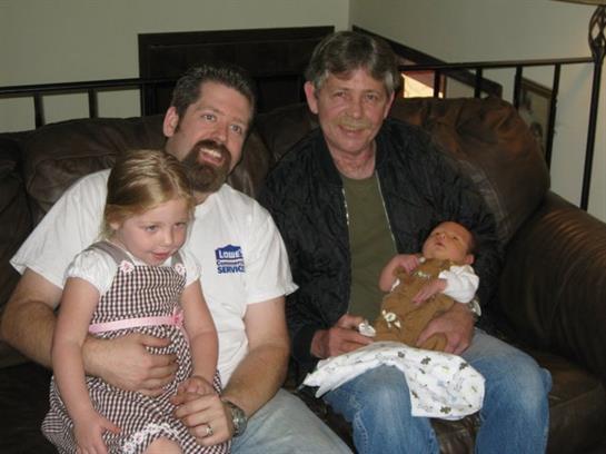 Two adults and two children sit together on a couch, enjoying a relaxed family moment.