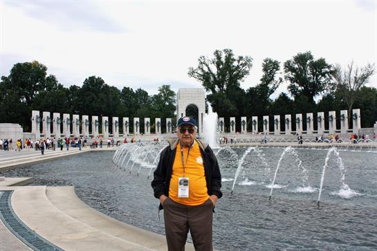 A proud veteran stands near the fountains of the World War II Memorial, reflecting on history.
