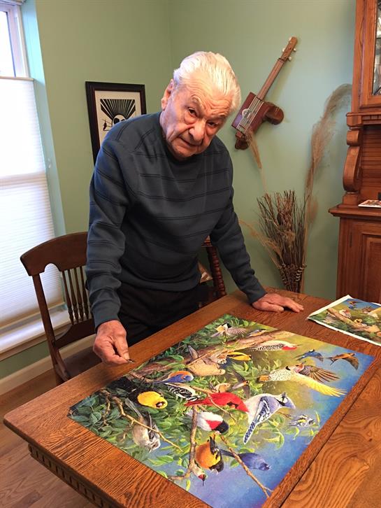 An elderly man intently assembles a vibrant puzzle, appreciating the intricate details indoors.