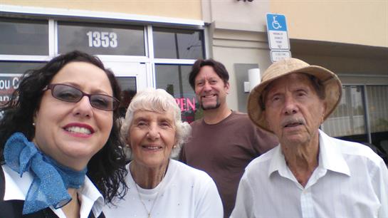 Four friends smile joyfully outside a store, enjoying the bright sunshine.